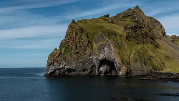 Under a bright blue sky, a huge rock, almost like an island, is exactly shaped as an elephant